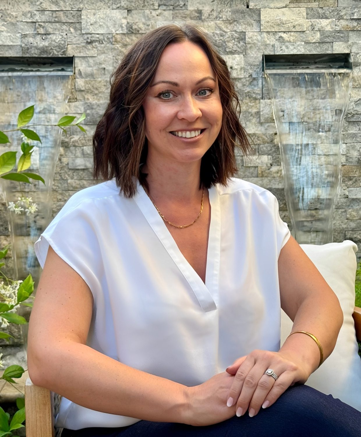 Smiling woman sitting outdoors near stone wall.